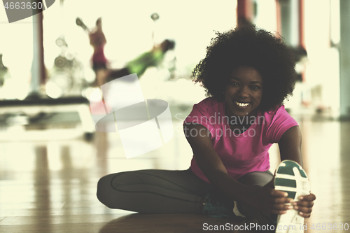 Image of woman in a gym stretching and warming up man in background worki