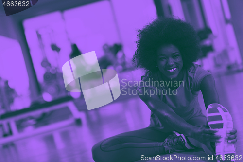 Image of woman in a gym stretching and warming up man in background worki