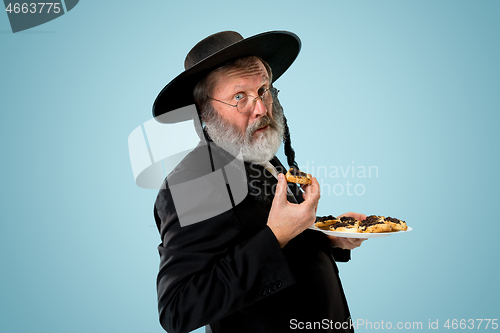 Image of The senior orthodox Jewish man with black hat with Hamantaschen cookies for Jewish festival of Purim