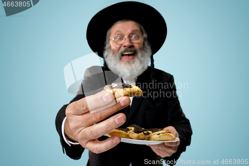 Image of The senior orthodox Jewish man with black hat with Hamantaschen cookies for Jewish festival of Purim