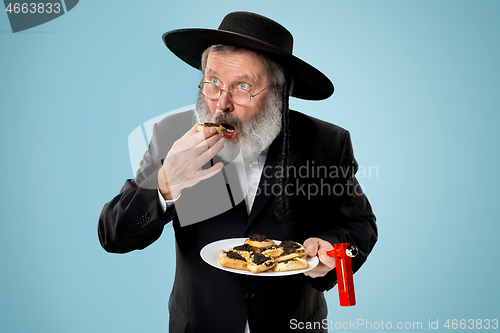 Image of The senior orthodox Jewish man with black hat with Hamantaschen cookies for Jewish festival of Purim