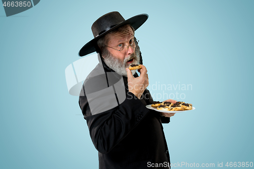 Image of The senior orthodox Jewish man with black hat with Hamantaschen cookies for Jewish festival of Purim