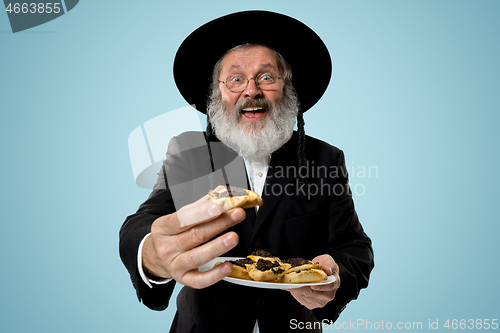 Image of The senior orthodox Jewish man with black hat with Hamantaschen cookies for Jewish festival of Purim