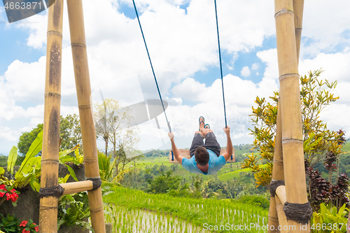 Image of Happy female traveller swinging on wooden swing, enjoying summer vacation among pristine green rice terraces.