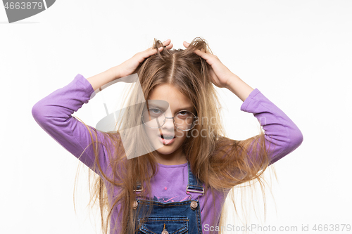 Image of Long-haired girl scratches her head with her hands