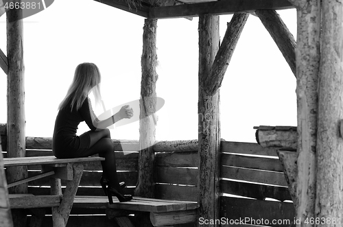 Image of A girl sits in a wooden arbor on a foggy day and looks into the distance