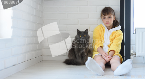 Image of The punished girl sits in the corner of the room, a large domestic cat sits nearby