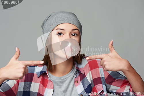 Image of Closeup of cheeky teen girl blowing bubblegum and pointing at it