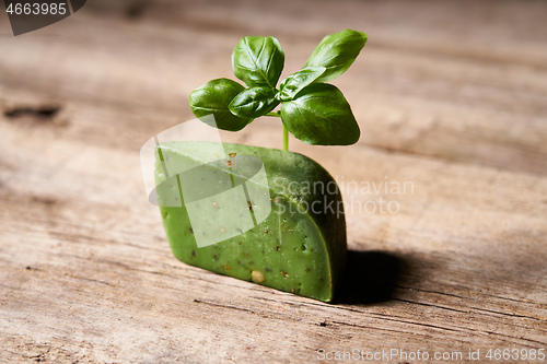 Image of A piece of gourmet basil cheese with twig of basil on rough wooden planks