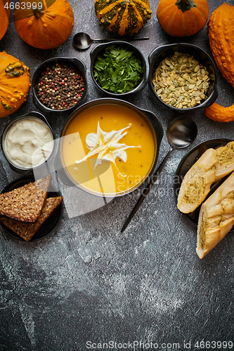 Image of Delicious pumpkin soup with cream, seeds, bread and fresh herbs 