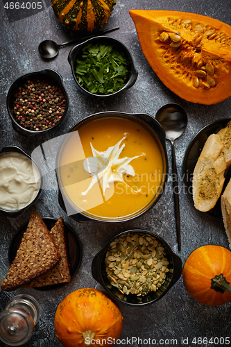 Image of Delicious pumpkin soup with cream, seeds, bread and fresh herbs in elegant ceramic black bowl