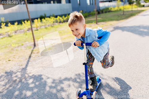 Image of happy little boy riding scooter in city