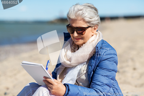 Image of senior woman writing to notebook on summer beach