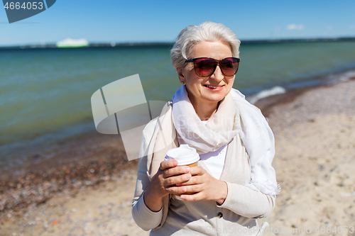 Image of senior woman drinking takeaway coffee on beach