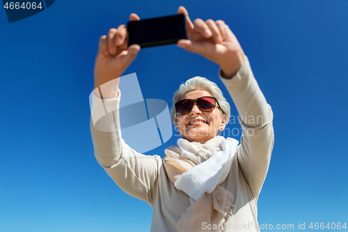 Image of senior woman taking selfie by smartphone outdoors