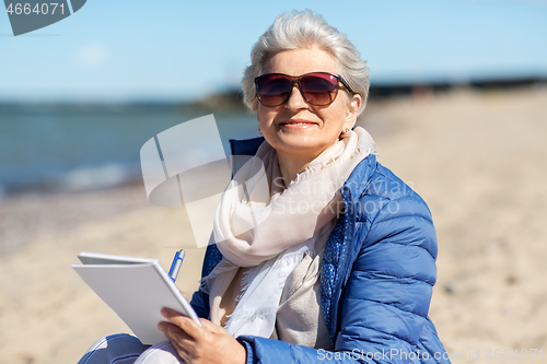 Image of senior woman writing to notebook on summer beach