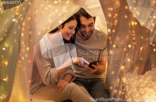 Image of happy couple with smartphone in kids tent at home