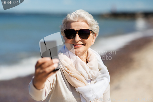 Image of senior woman taking selfie by smartphone on beach