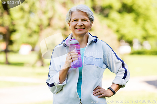 Image of sporty senior woman with bottle of water at park