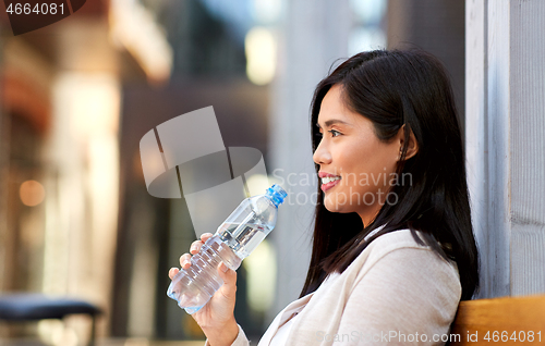 Image of woman drinking water sitting on wooden city bench