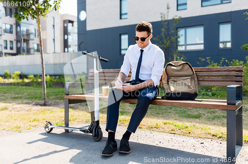 Image of smiling businessman writing to notebook in city