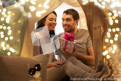 Image of happy couple with gift box in kids tent at home