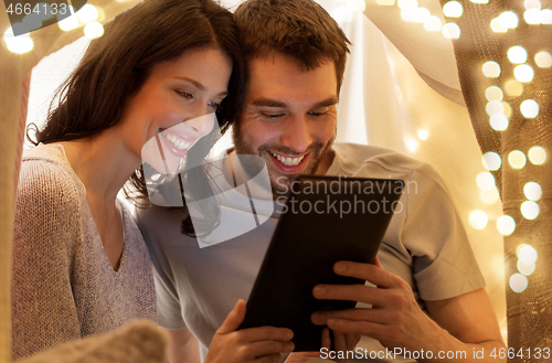 Image of happy couple with tablet pc in kids tent at home