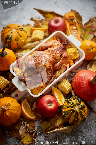 Image of Thanksgiving dinner table with roasted whole chicken or turkey, pumpkin, baked potatoes, chestnuts