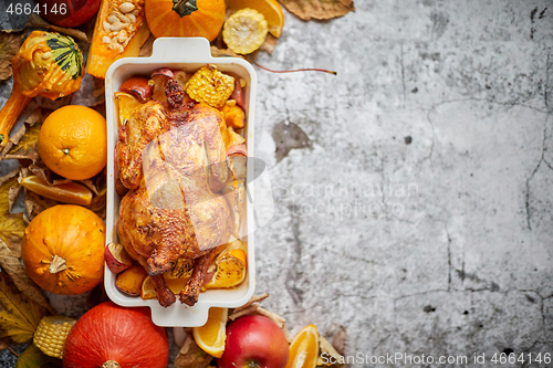 Image of Thanksgiving dinner table with roasted whole chicken or turkey, pumpkin, baked potatoes, chestnuts