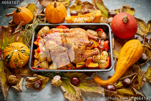 Image of Roasted chicken or turkey garnished with pumpkins, pepper and potatoes. Served on a rustic table