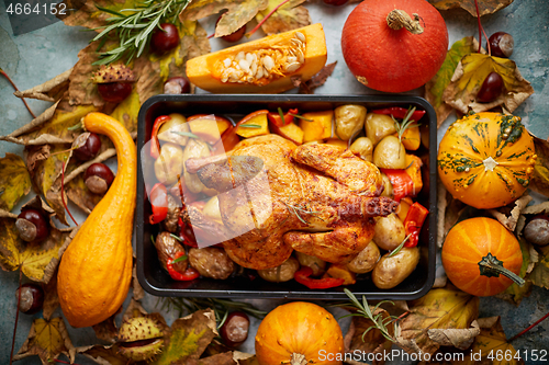 Image of Roasted chicken or turkey garnished with pumpkins, pepper and potatoes. Served on a rustic table