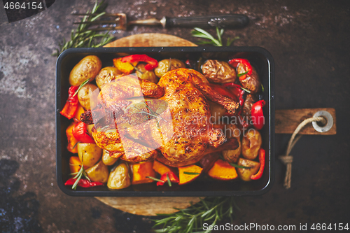 Image of Delicious whole chicken cooked with pumpkin, pepper and potatoes. Served in metal baking pan.