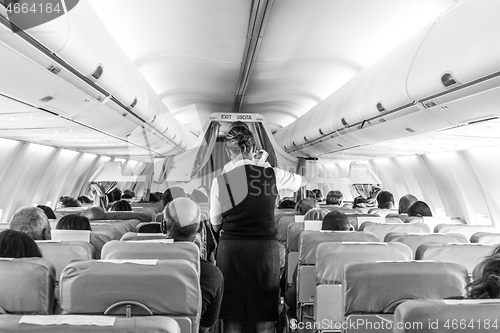 Image of Interior of commercial airplane with stewardess serving passengers on seats during flight.