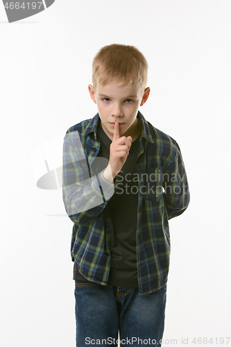 Image of Portrait of teenager boy showing quieter sign, pressing index finger to his mouth