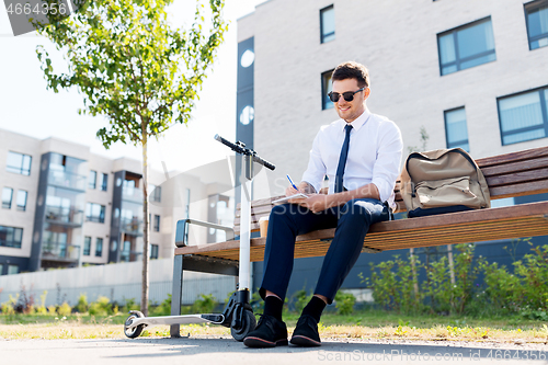 Image of smiling businessman writing to notebook in city