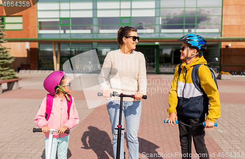 Image of happy school children with mother riding scooters