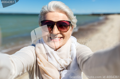 Image of senior woman in sunglasses taking selfie on beach