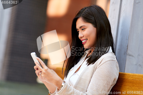 Image of asian woman using smartphone sitting on bench