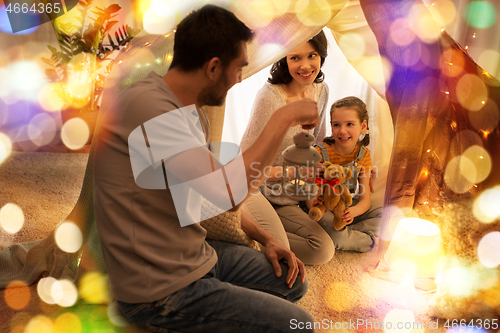 Image of happy family playing in kids tent at night at home