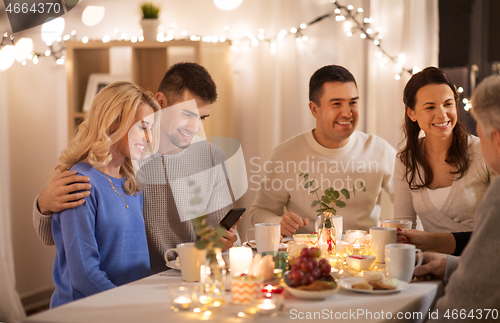 Image of happy family with smartphone at tea party at home
