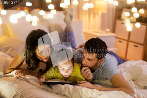 Image of family with tablet pc in bed at night at home