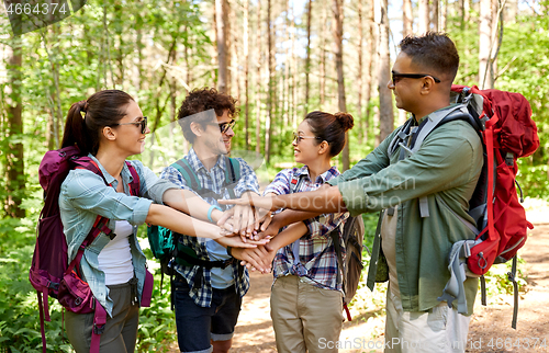 Image of friends with backpacks stacking hands in forest