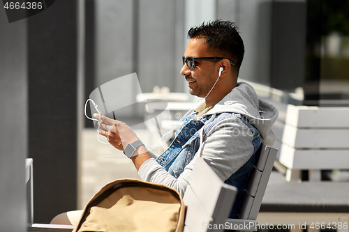 Image of man with earphones and smartphone on city street