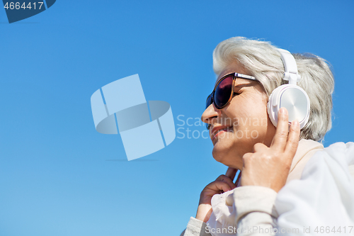 Image of old woman in headphones listens to music outdoors
