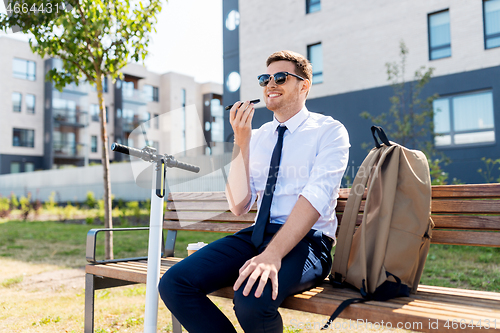 Image of businessman recording voice message by smartphone