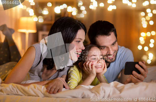 Image of happy family with smartphone in bed at night