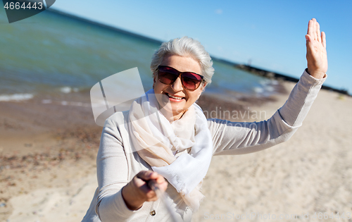 Image of old woman taking selfie and waving hand on beach
