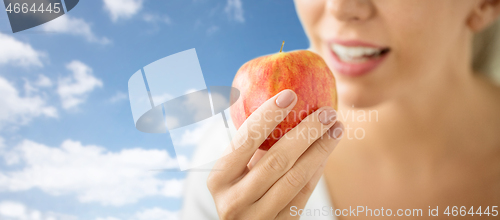 Image of close up of woman holding ripe red apple over sky