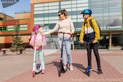 Image of happy school children with mother riding scooters