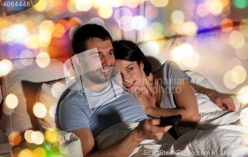 Image of happy couple watching tv in bed at night at home